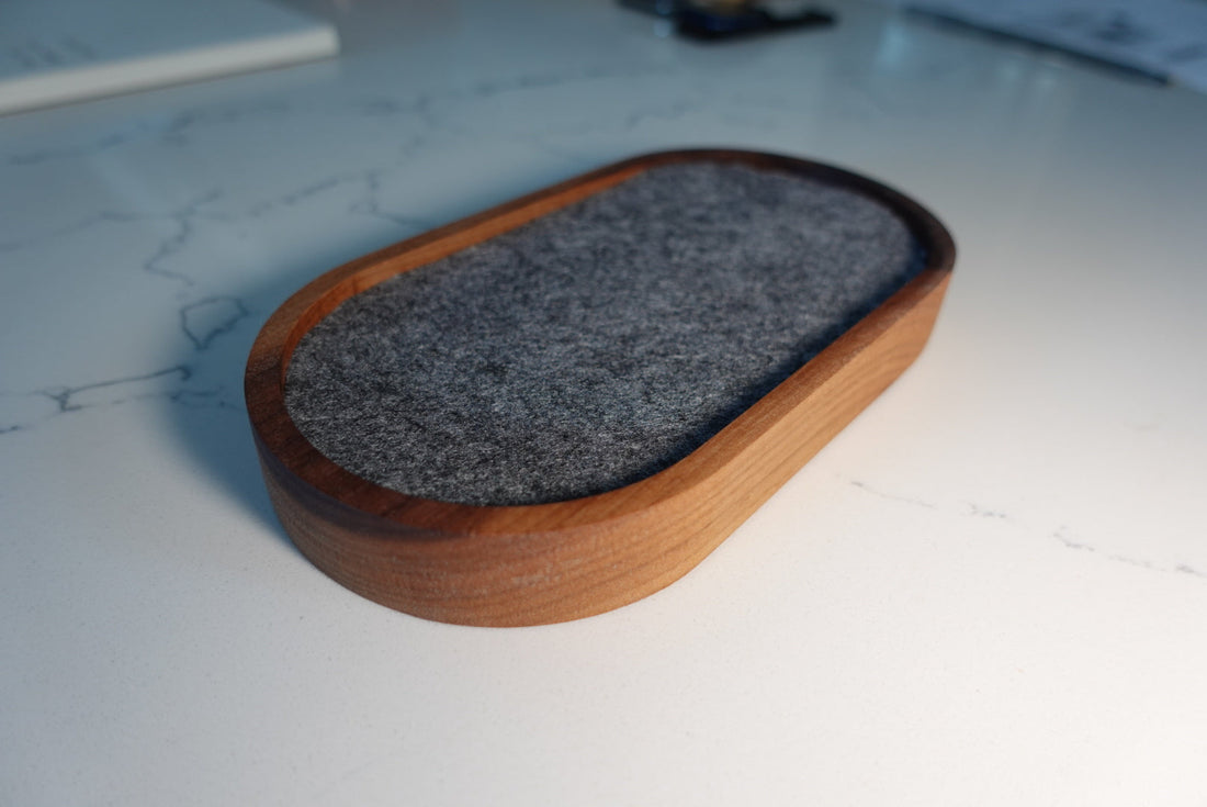 Rounded wooden catchall tray with grey felt lining on a pale stone surface