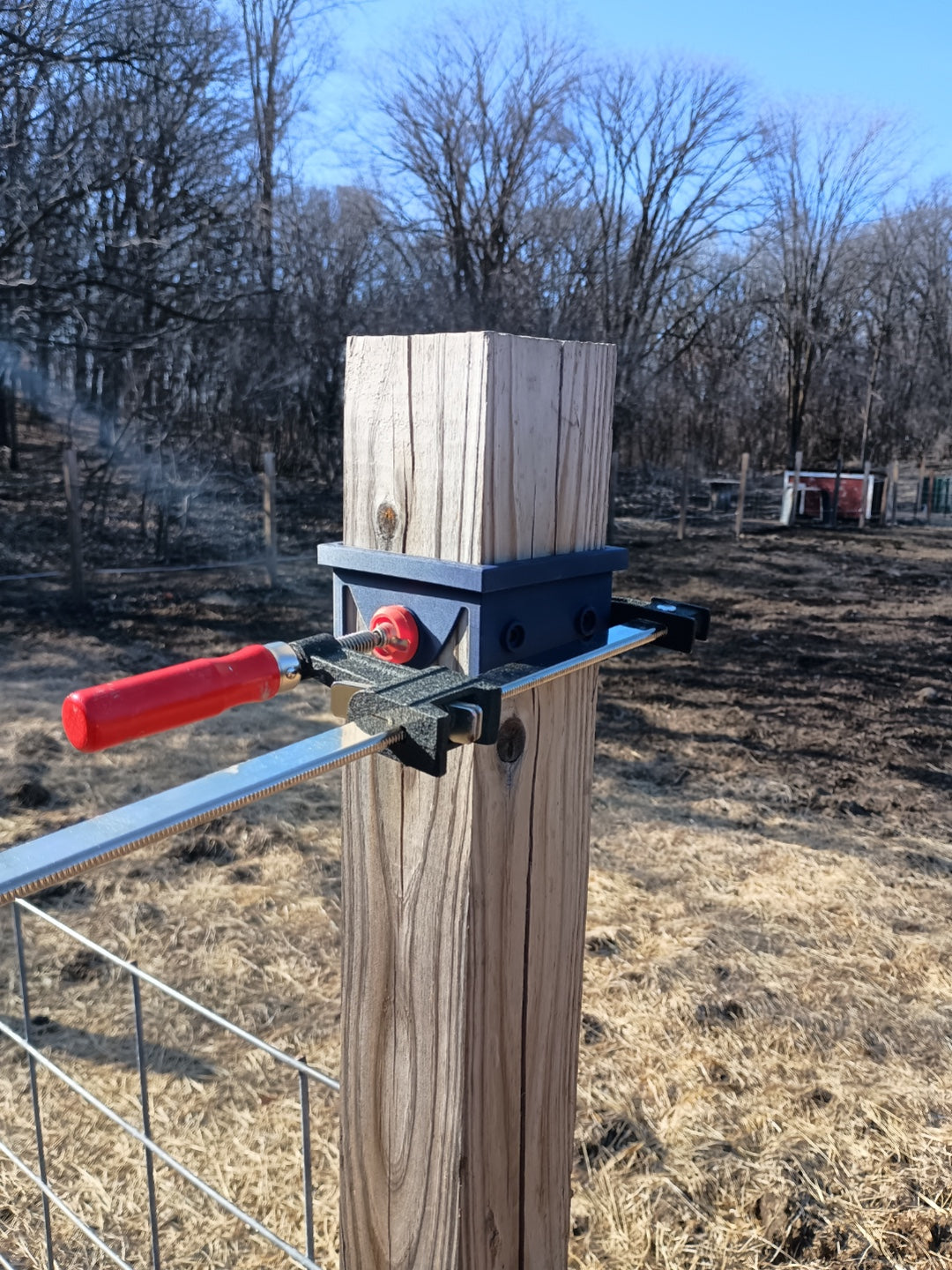 Black 3D printed circular saw guide secured around a square wooden fence post with a bar clamp