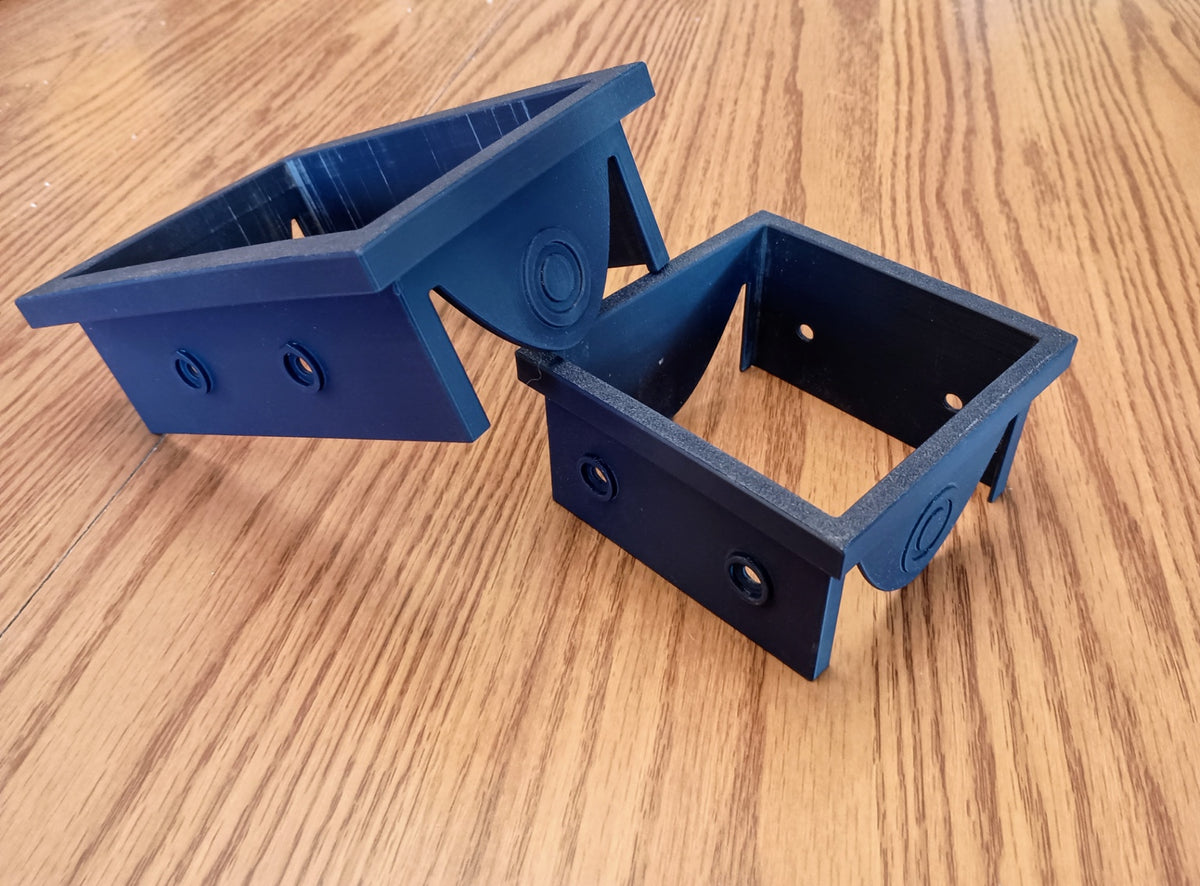 Two black 3D printed circular saw cutting guides for 4x4 and 4x6 wooden fence posts on a tabletop